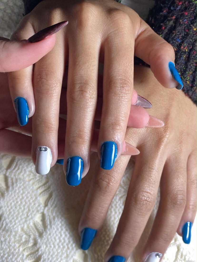 Unhas em azul petróleo com uma unha branca decorada com pedrarias